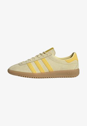 Baskets basses en daim beige avec trois bandes jaunes, lacets et semelle en gomme, vues de côté.