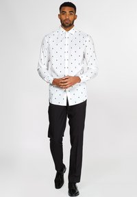 Camicia bianca button-up con motivi di alberi verdi, maniche lunghe e colletto a punta, abbinata a pantaloni neri e scarpe lucide.