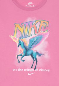 T-shirt rose arborant un graphique coloré d'une licorne ailée, avec le texte en gras "NIKE" au-dessus et "sur les ailes de la victoire" en dessous.