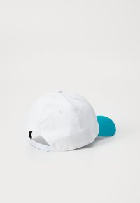 Hvit baseballcap med en turkis brem. Har en teksturert overflate, ventilasjonsåpninger og et justerbart belte bak.
