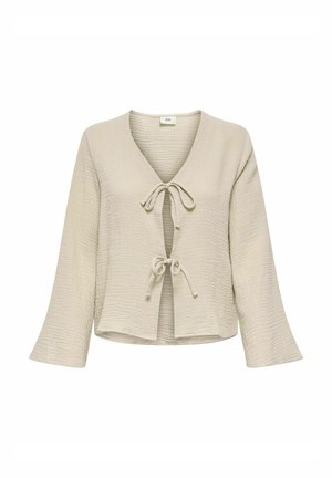 Haut enveloppant texturé beige clair avec un col en V, comportant deux attaches à nouer à l'avant et des manches longues légèrement évasées.