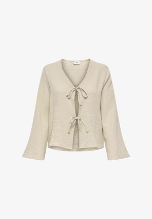 Haut enveloppant texturé beige clair avec un col en V, comportant deux attaches à nouer à l'avant et des manches longues légèrement évasées.