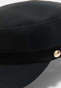 Cappello in lana nera con cima strutturata, texture liscia e un dettaglio in metallo dorato sul lato.