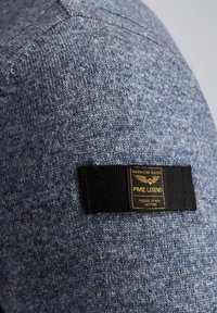 Maglione in tessuto texturizzato blu con un'etichetta nera e lettering dorato. L'etichetta recita 'PME LEGEND', con un motivo di design e dettagli di cucitura.