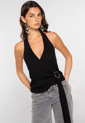 Mujer con top halter negro con detalle de hebilla lateral y vaqueros grises con tachuelas, complementado con grandes pendientes de aro plateados.
