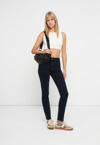 Fekete keresztpántos táska, fehér crop top, sötétkék szűk farmernadrág és bézs, leopárdmintás sportcipő. Simább textúrák és egyszerű dizájn.