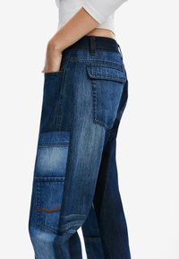 Cargo-Jeans aus Denim in verschiedenen Blautönen, mit lockerer Passform, großen Seitentaschen und kontrastierenden Nähten an den Säumen.