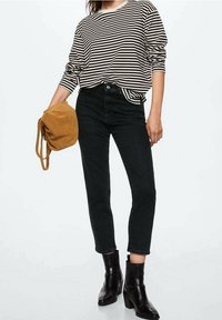 Haut à manches longues rayé avec un col rond, associé à un jean noir et des bottines noires. Sac en suède marron tenu dans la main gauche.