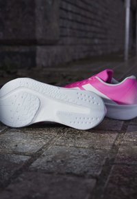 Chaussures de sport roses avec un dessus texturé, semelle en caoutchouc blanche et motif de traction. Présentent des lacets et un design de talon lisse.