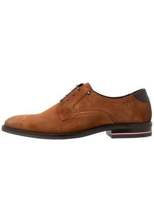 Chaussure habillée pour homme en daim marron avec talon marron foncé, design à lacets et semelle basse empilée avec un accent rayé rouge, blanc et bleu.