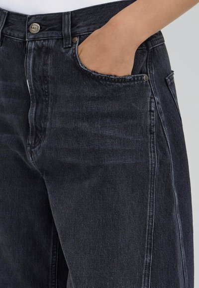 Tumši džinsi ar augstu jostasvietu, taisnu piegriezumu un vienu priekšējo kabatu. Audumam piemīt smalka tekstūra un mazliet izbalējusi krāsa.