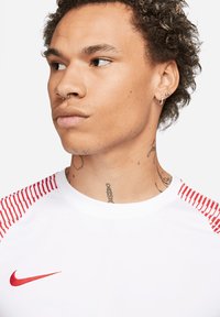 Wit sportshirt met rode gestreepte accenten op de schouders, voorzien van een klein rood Nike-logo op de borst.