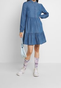 Sinine džinsikleit, pikad varrukad, krae, kihiline seelik ja lõdvestatud lõige, millele on sobitatud sidumiskreppide sokid ja spordijalatsid.