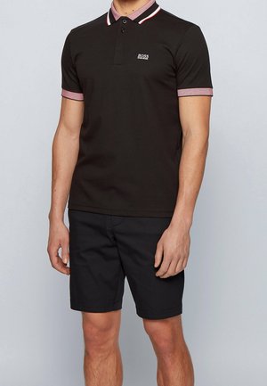 Schwarzes Poloshirt mit kontrastierendem Kragen und Ärmelenden. Verfügt über ein kleines Logo auf der Brust. Kombiniert mit schwarzen Shorts.