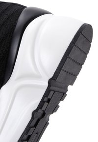 Close-up of a black and white sneaker sole showing textured black rubber tread and smooth white midsole details.
