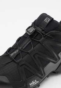 Close-up of black trail running shoe with elastic laces, toggle fastener, mesh upper, and textured sole labeled M&S Contagrip.