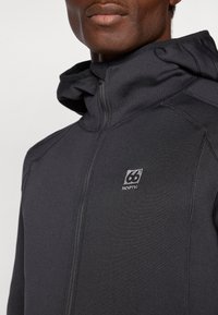 Felpa nera con zip e cappuccio, realizzata in tessuto liscio. Presenta cuciture a contrasto e una patch con logo sulla parte sinistra del petto.