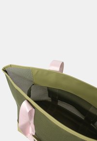 Borsa a rete verde oliva con manici in tessuto rosa. Presenta un ampio interno e una forma strutturata, adatta per trasportare vari oggetti.