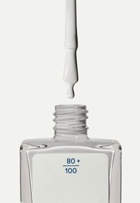 Heldere glazen nagellakfles met een witte applicatortip en een druppel witte lak; heeft een etiket met blauwe tekst "80+" en "100."