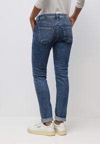 Vaqueros de denim azul ajustados con una cintura de altura media, dos bolsillos traseros y puños enrollados, combinados con zapatillas blancas. Textura suave y diseño clásico.