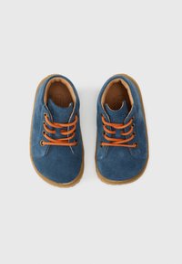 Kék velúr cipők narancssárga fűzőkkel, kerek orral és barna gumitalppal. Texturált felsőrész és varrott részletek az oldaluk mentén.