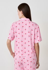 Camicia a maniche corte rosa con strisce verticali bianche, caratterizzata da un motivo a stampa di ciliegie. Il materiale sembra leggero e liscio.