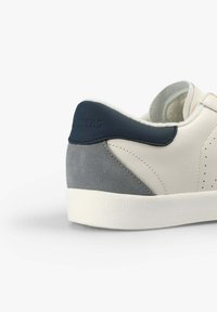 White leather sneaker with navy and gray suede accents. Features perforated design, padded collar, and textured rubber sole.