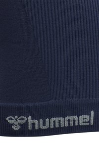 Tissu tricoté côtelé bleu marine avec un logo « hummel » gris tissé et un emblème d’abeille le long du bord inférieur.