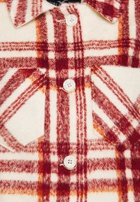 Röd och krämfärgad rutigt knapp-up skjorta med ett mjukt, strukturerat tyg, som har två framfickor och vita knappar.