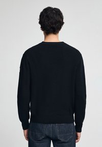 Zwart gebreid sweater met een geribbelde textuur, ronde hals en lange mouwen. De achterkant heeft een naadloos ontwerp en een elastische zoom.