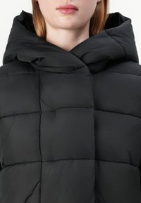 Casaco puffer preto com capuz alto e dobrado; possui um design acolchoado, textura suave e fecho com botões.