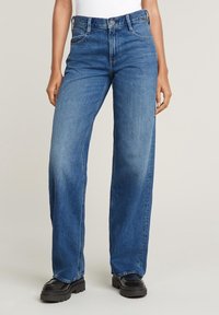 Bredbeniga blå denimjeans med hög midja, med sydda fickor, knäppning fram och lätt urblekta områden för en avslappnad look.