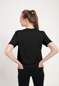 Schwarzes Baumwoll-T-Shirt mit kurzen Ärmeln, Rundhalsausschnitt und lockerer Passform. Getragen mit dunklen Jeans; schlichtes Design ohne sichtbare Logos oder Muster.