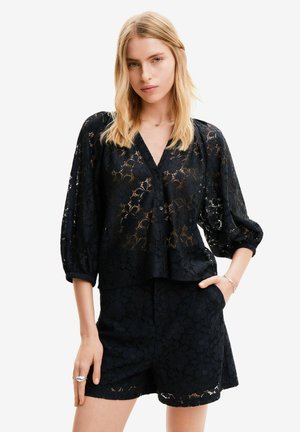Blusa nera in pizzo con maniche a sbuffo, scollo a V e chiusura con bottoni. Motivo floreale testurizzato su tutto il capo, abbinata a pantaloni corti neri coordinati.