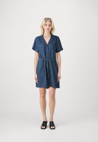 Denim skjortekjole med korte ermer, knapper foran, to brystlommer og belte i livet; har en avslappet passform og en mørkeblå nyanse.