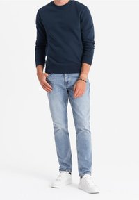 Mörkblå sweatshirt med rund halsringning; lättviktsmaterial. Ljusblå jeans; figurnära design med subtila blekningar. Vita sneakers.