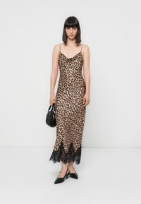 Vestido slip de cetim com padrão de leopardo, decote drapeado, com rendinha na bainha e alças finas ajustáveis. Usado com uma bolsa preta e sapatos de salto.