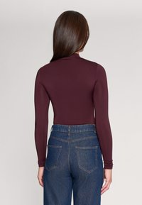 Bodysuit z długim rękawem, dopasowany, w burgundowym kolorze, połączony z niebieskimi dżinsami z wysokim stanem, z tylnymi kieszeniami i wyraźnie zaznaczoną talią.