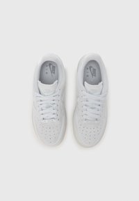 Ténis brancos com parte superior em camurça, biqueira perfurada e sola de borracha lisa. Apresentam atacadores tonais e um logótipo subtil na língua.