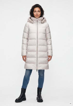 Woman standing wearing a light beige padded winter coat with hood, blue jeans, and black ankle boots on a white background.