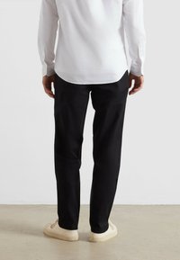 Witte longsleeve blouse, recht gesneden zwarte broek en lichtbeige schoenen. Gladde textuur, met een klassieke shirtkraag en knoopdetails.
