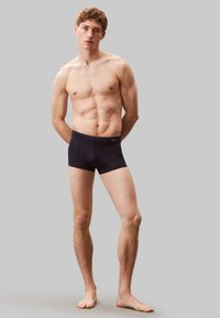 Męskie ciemnogranatowe bokserki o gładkiej fakturze i szerokiej elastycznej talii. Model stoi boso na szarym tle.