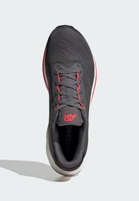 Gray athletic shoe with a textured upper and red accents. Features a lace-up design, padded collar, and a contrasting white sole.