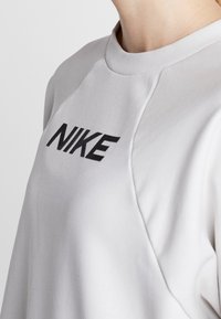 Sweat-shirt gris clair à col rond avec logo "NIKE" noir ; présente des manches raglan et un matériau en coton lisse avec une texture douce.