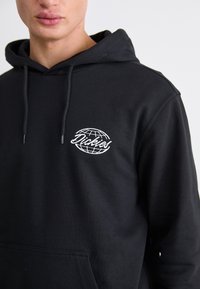 Sudadera negra de mezcla de algodón, con un logotipo de globo blanco y texto en el lado izquierdo del pecho. La tela es suave y tiene un corte holgado.