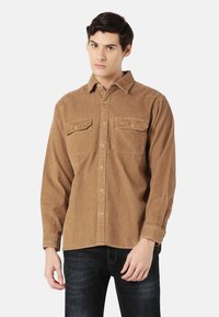 Brown corduroy shirt with a button-down collar, two chest pockets, and a ribbed texture. Paired with dark jeans.