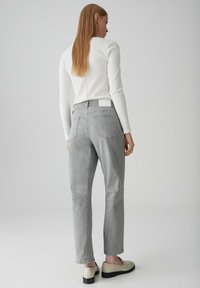 Jeans grigi con taglio dritto, cuciture visibili, tasche laterali e una toppa bianca sul retro. Abbinati a mocassini beige.