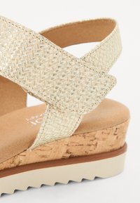 Platform sandal with crisscross braided metallic gold straps, cushioned tan footbed, and a cork-textured wedge heel with a rubber sole.