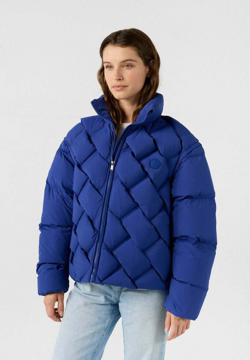 Blaues Puffer Jacket mit diamantgequiltem Design, hohem Kragen und Reißverschluss. Verfügt über ein Logo auf der Brust und übergroße Ärmel.