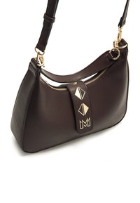 Braune Ledertasche mit geschwungener Form, ausgestattet mit einem goldenen Reißverschluss und geometrischen Metallakzenten auf der Vorderseite. Verstellbarer Schultergurt inklusive.